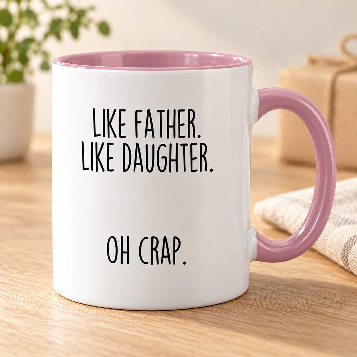 Like Father, Like Daughter, Oh Crap coffee mug — Pink variant, photographed on an oak table.